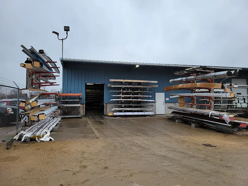 Exterior of a blue warehouse with materials being stored outside.