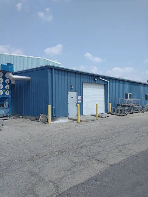 Exterior view of large blue warehouse facility with a dock door and employee entrance.