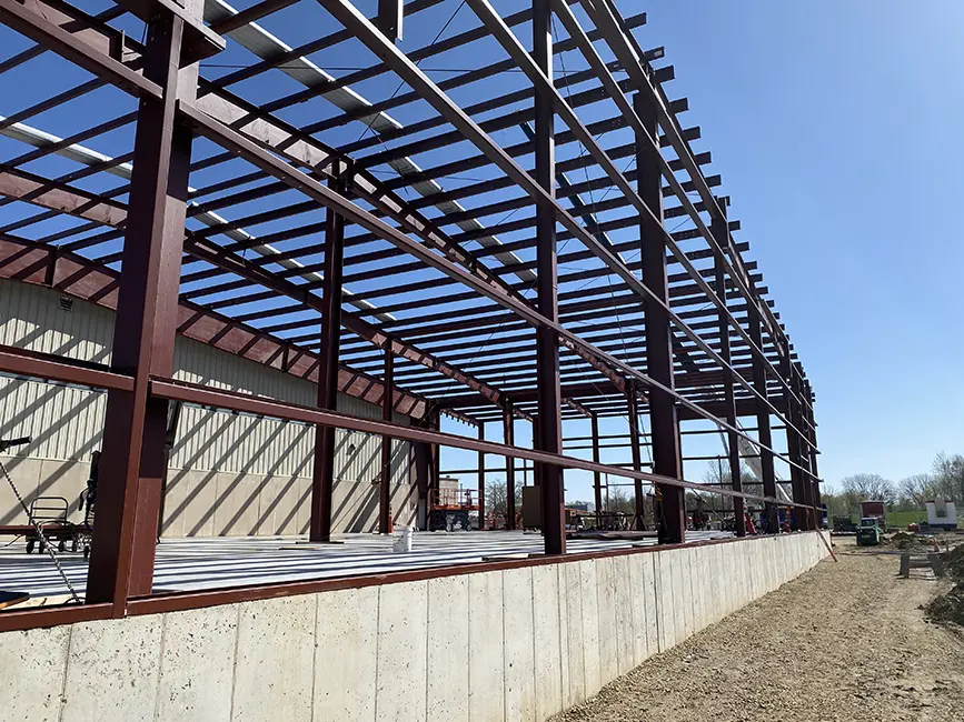 Steel frame structure of a warehouse under construction with clear blue skies in the background.